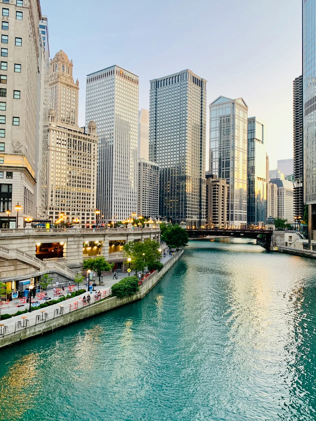 The Chicago Riverwalk at golden hour, with towers reflected in green water.