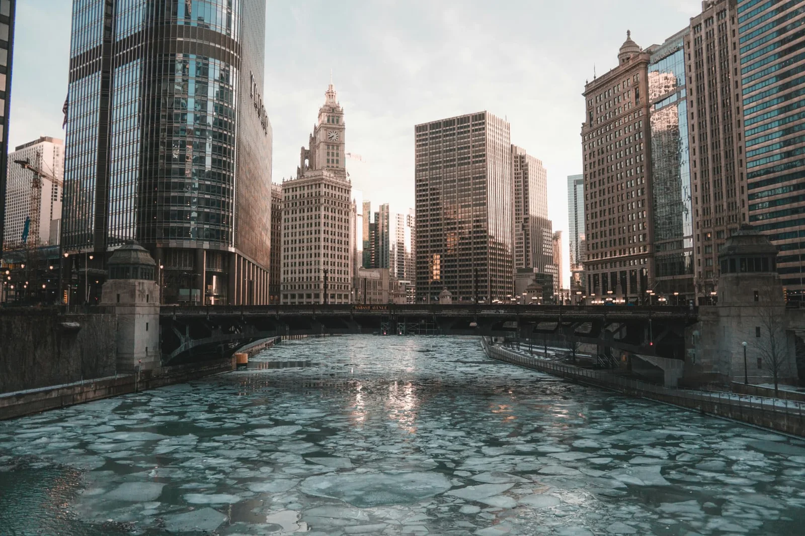Chicago River in winter, covered in floating ice, between downtown towers and a bridge.